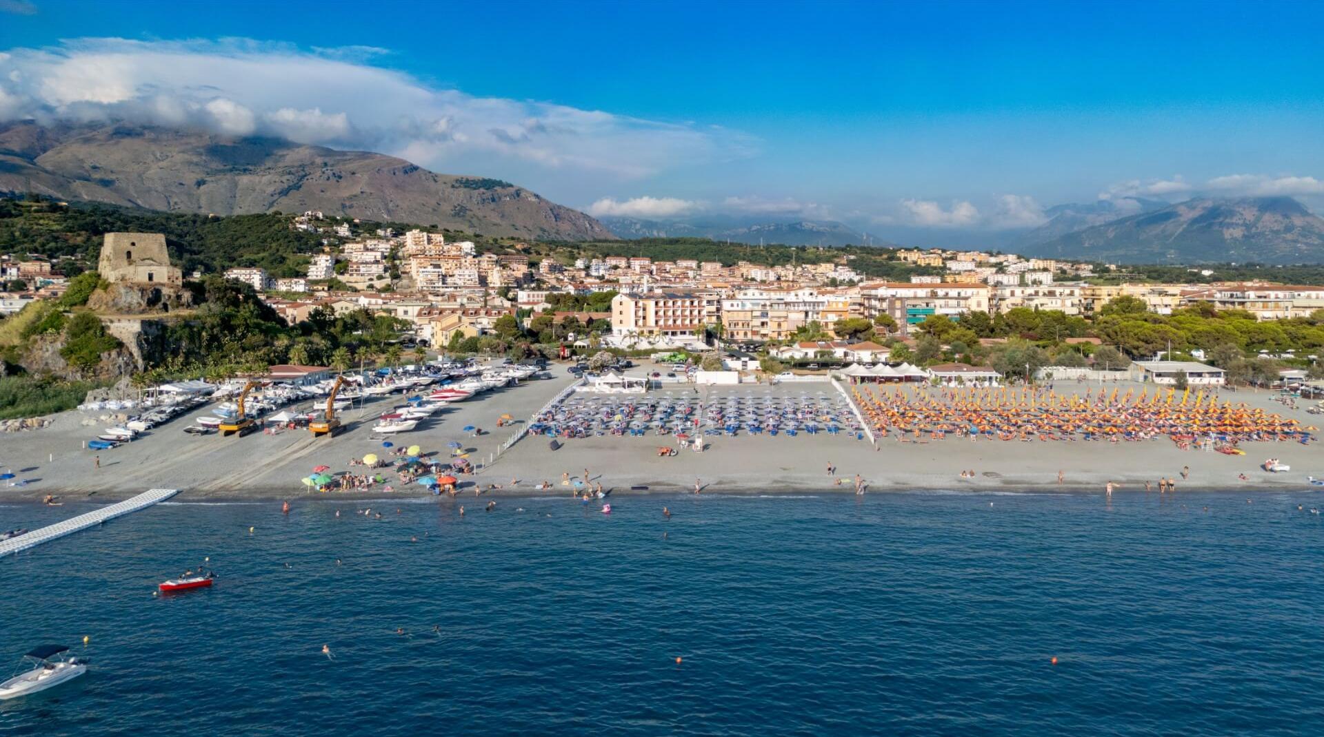 Spiaggia affollata con ombrelloni colorati e vista su montagne e città costiera.