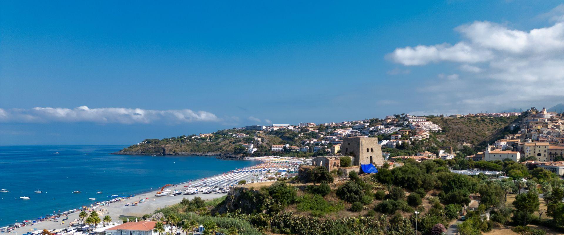 Vista panoramica di una spiaggia con mare azzurro e un'antica torre in pietra.