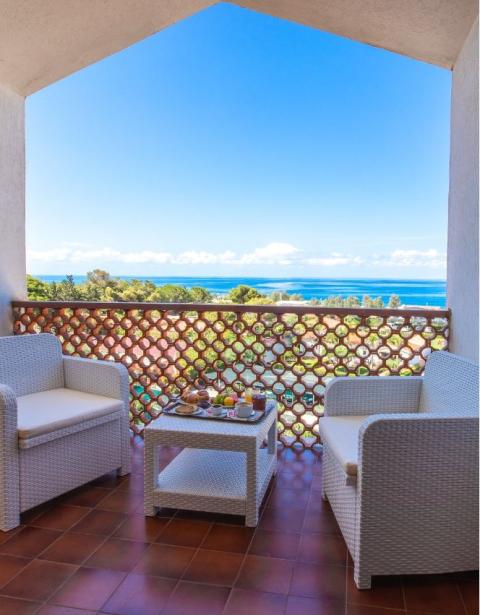 Terrazza con vista mare, arredi bianchi e colazione su tavolino.