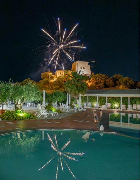 Fuochi d'artificio sopra un castello, riflessi nella piscina di un resort notturno.