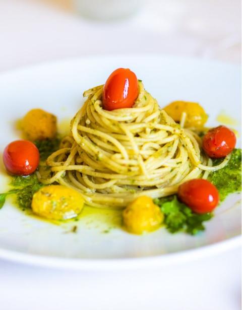 Spaghetti al pesto con pomodorini e crema di basilico su piatto bianco.