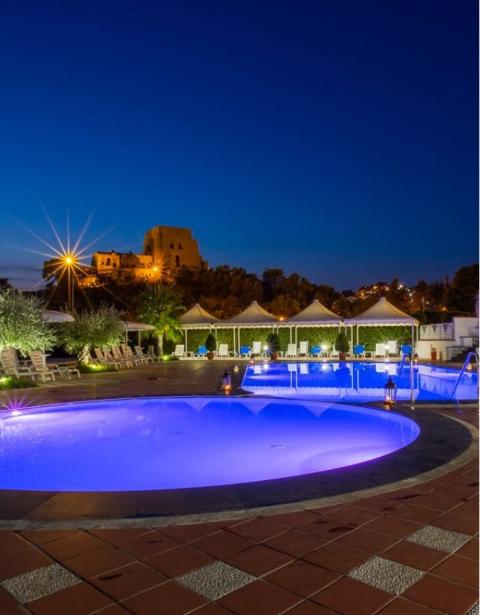 Piscina illuminata di notte con vista su un edificio storico sullo sfondo.