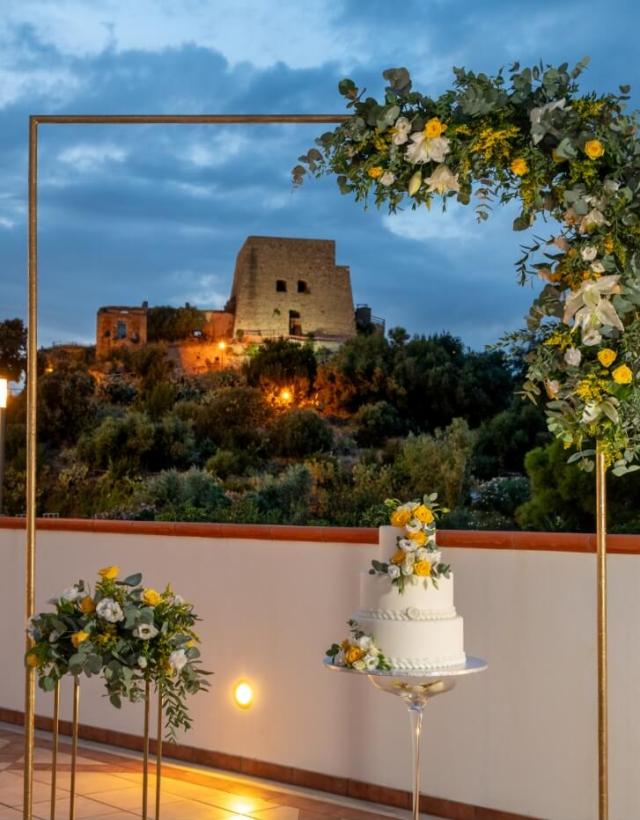 Torta nuziale con decorazioni floreali, vista su un castello al tramonto.